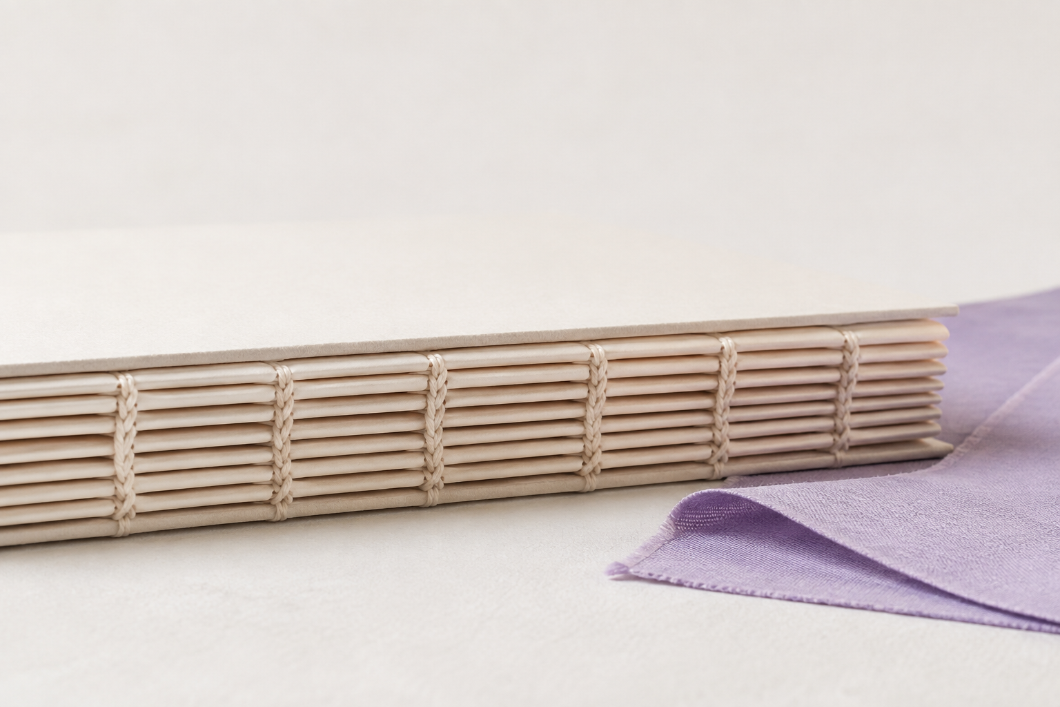 Detalhe da costura de um livro, com cadernos de papel e tecido lavanda.